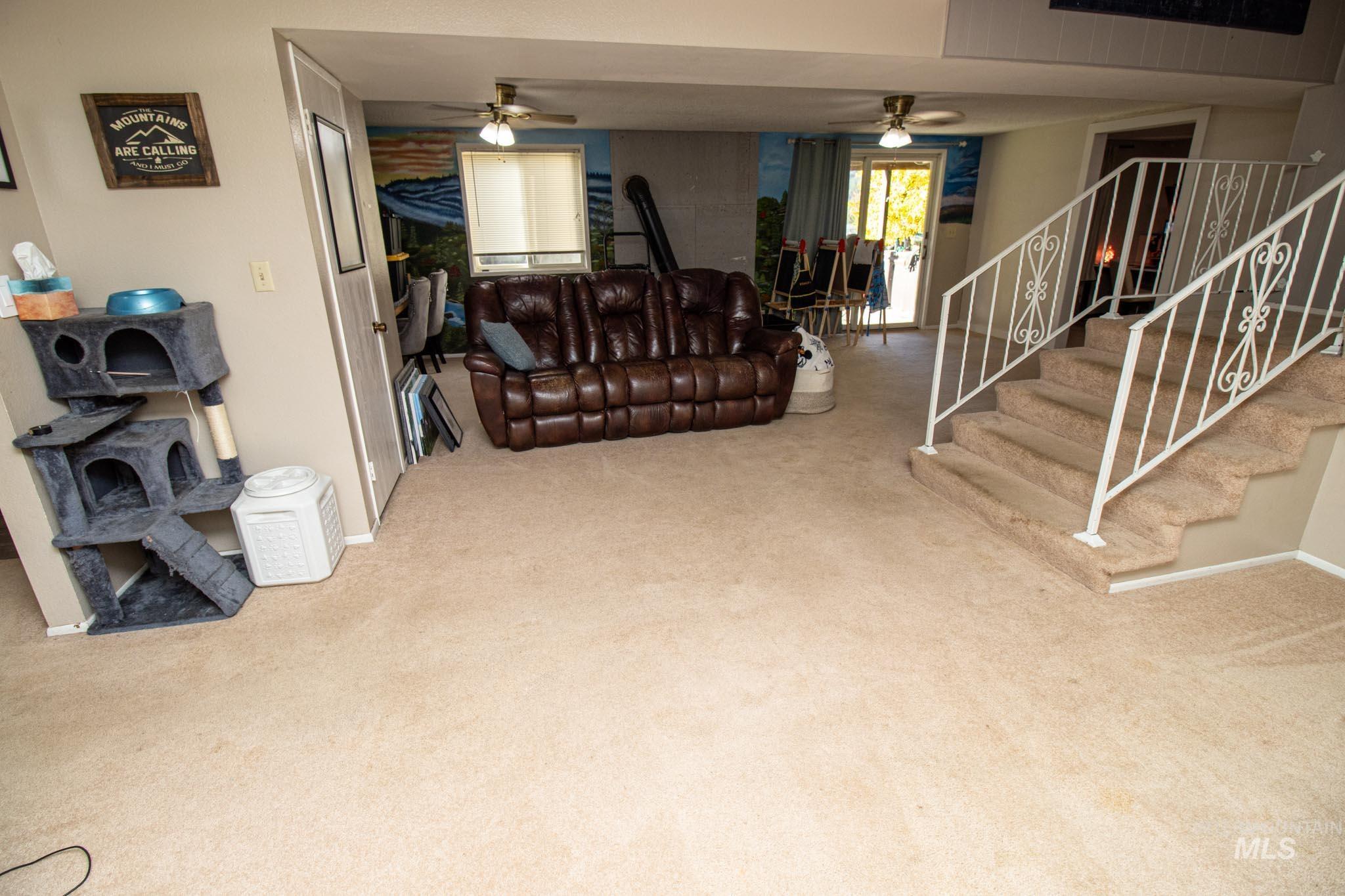 Living room with a ceiling fan, light colored carpet, and stairway