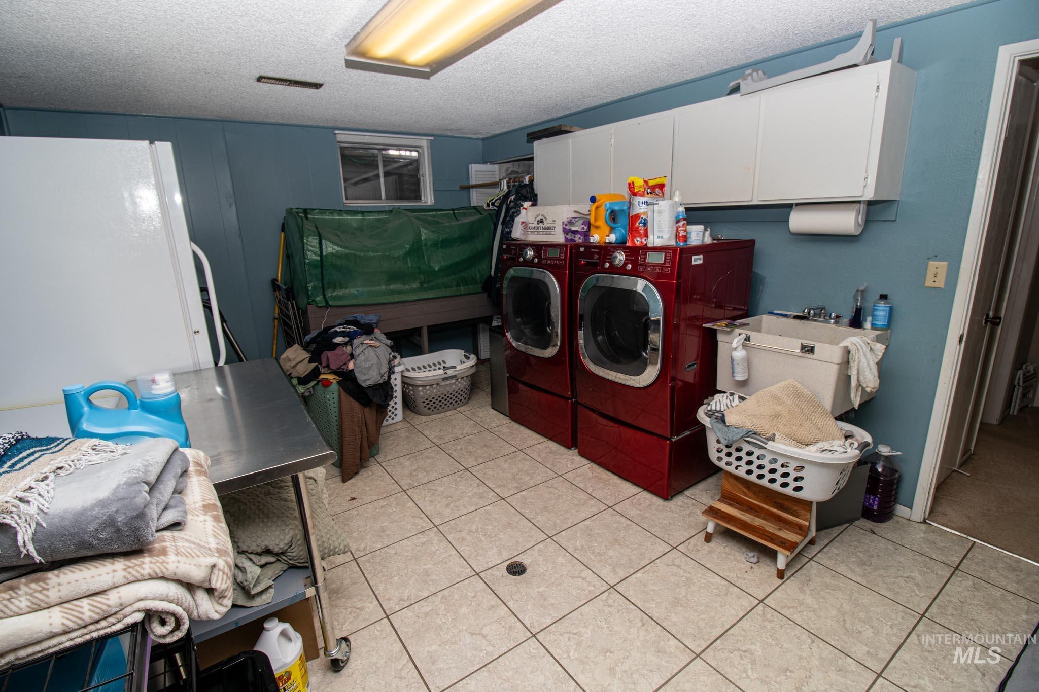 Washroom featuring a textured ceiling, light tile patterned floors, separate washer and dryer, and cabinet space