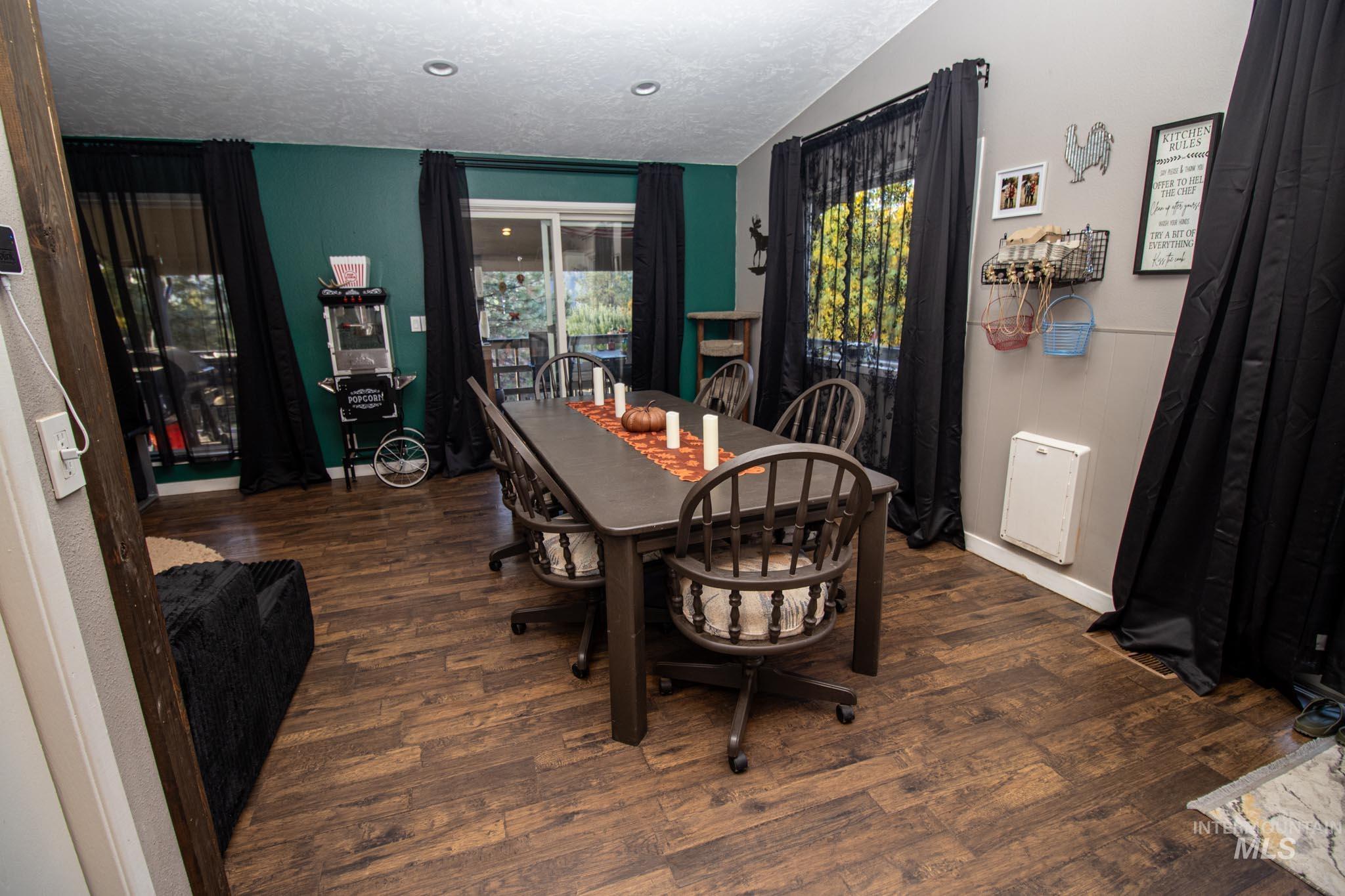 Dining room featuring dark wood-style floors, vaulted ceiling, and a textured ceiling
