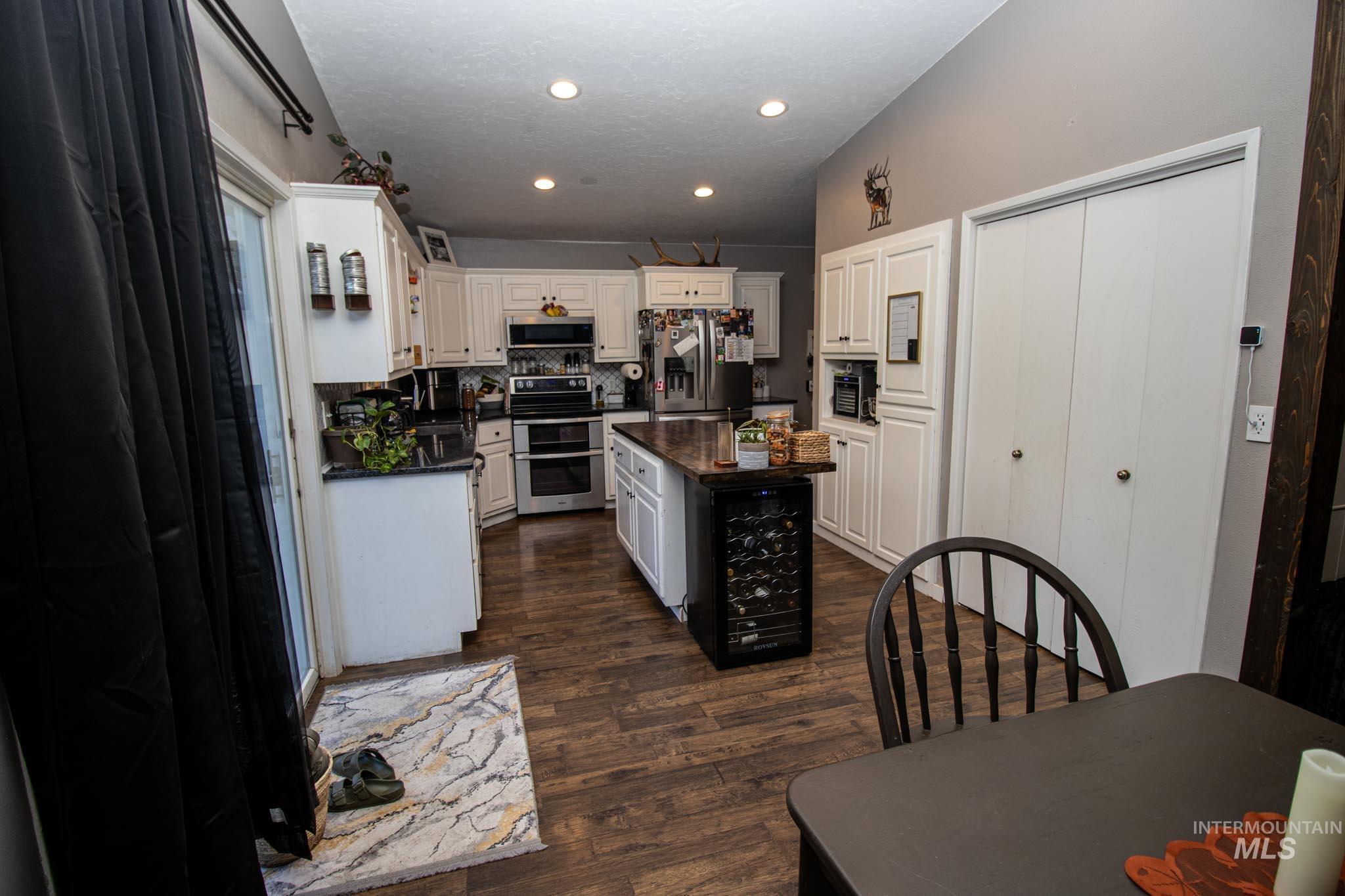 Kitchen featuring tasteful backsplash, a kitchen island, stainless steel appliances, dark wood-style floors, and white cabinetry