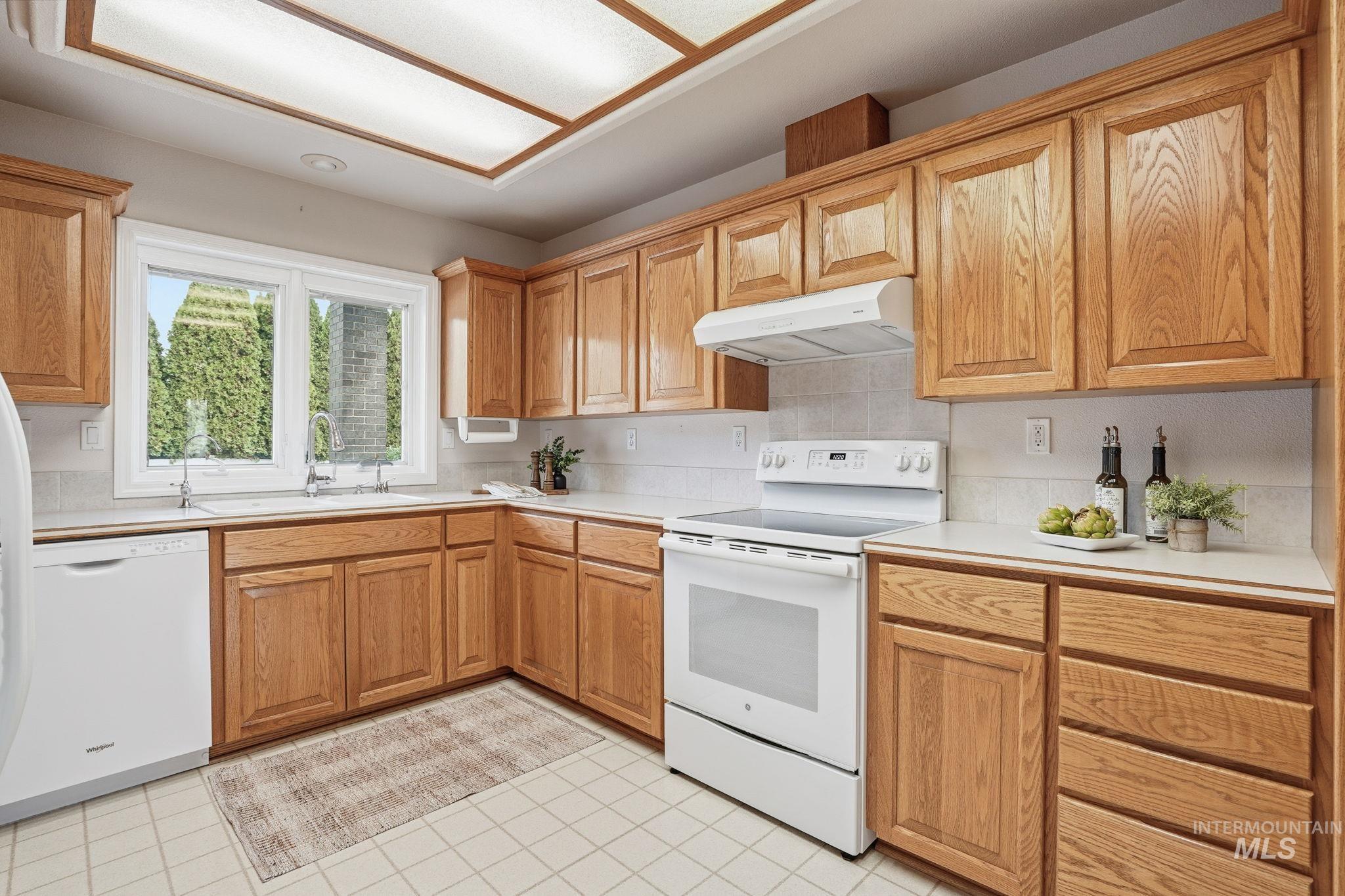Kitchen featuring white appliances, light countertops, and under cabinet range hood