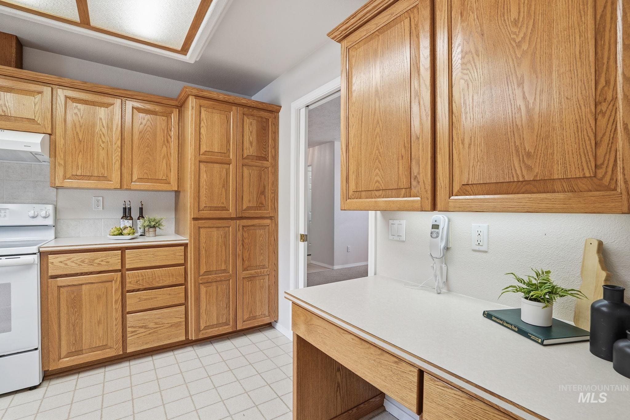 Kitchen featuring light countertops, white electric stove, light tile patterned flooring, under cabinet range hood, and brown cabinets