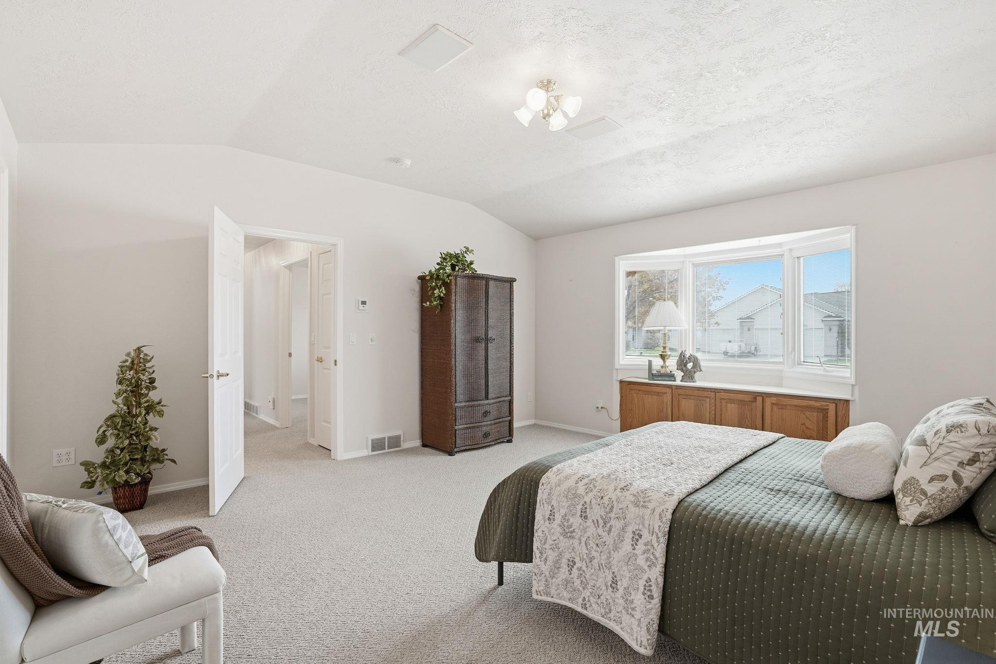 Primary bedroom featuring lofted ceiling and light carpet