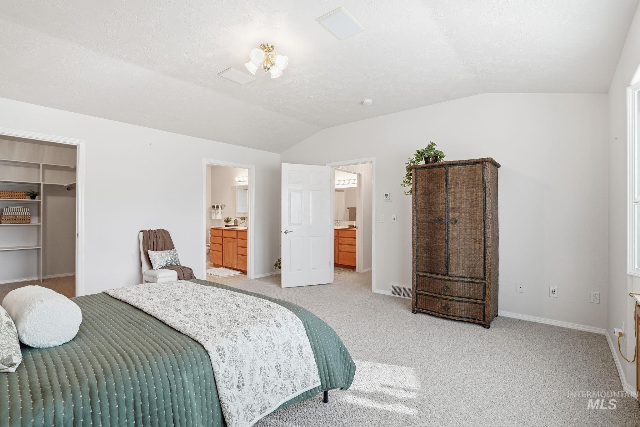 Primary Bedroom with lofted ceiling, a spacious walk-in closet, light carpet, and ensuite bathroom