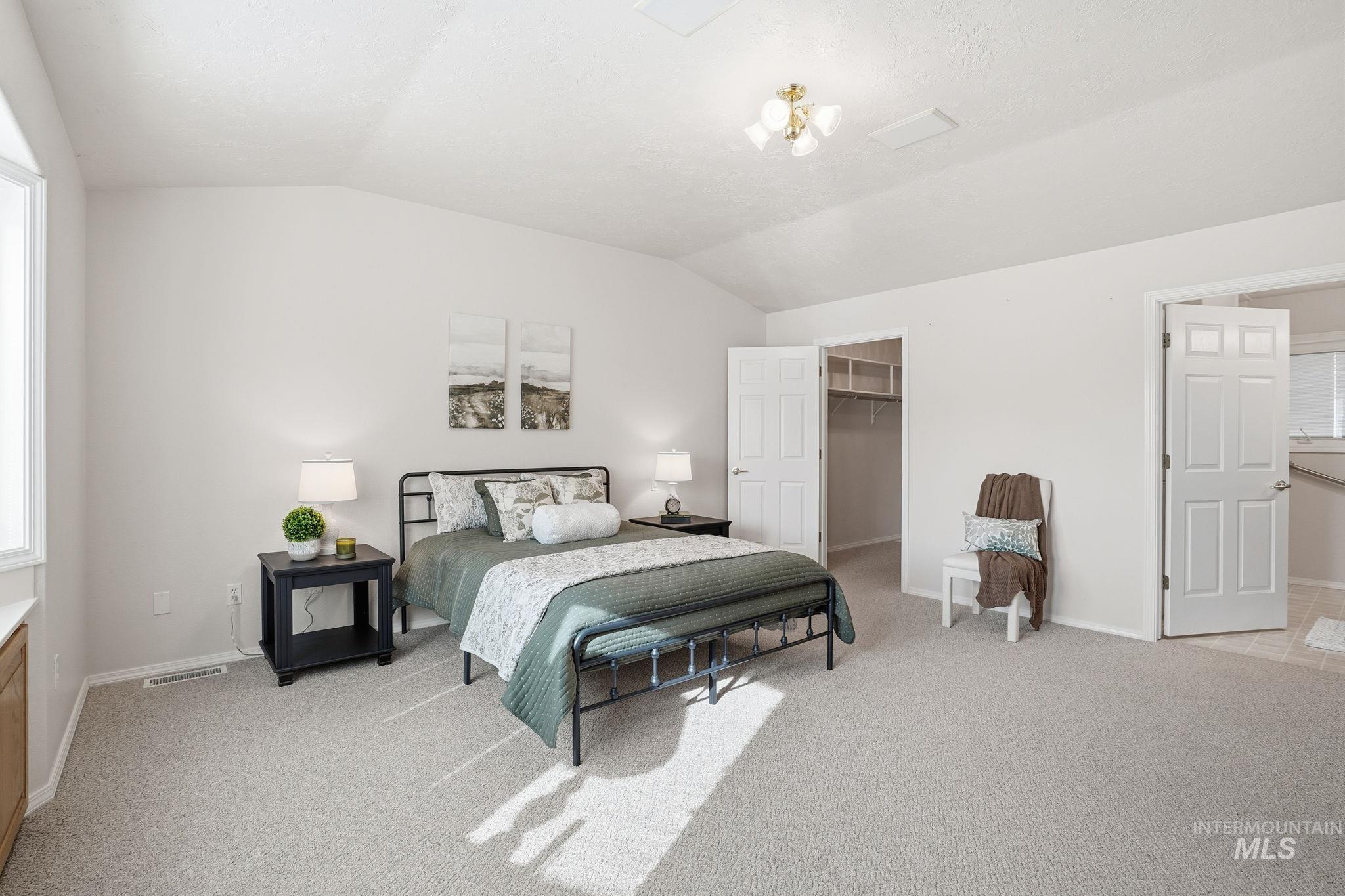 Primary Bedroom with vaulted ceiling, a spacious walk-in closet, and light colored carpet