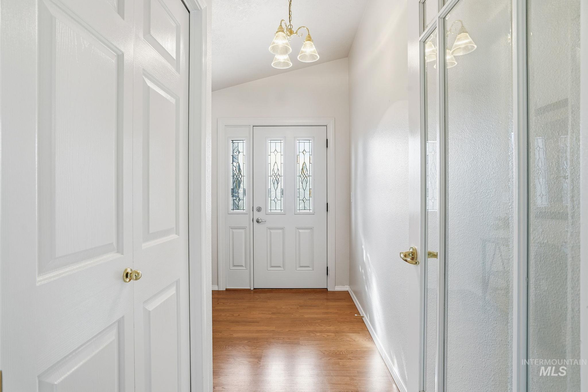 Doorway with lofted ceiling, wood finished floors, and a chandelier