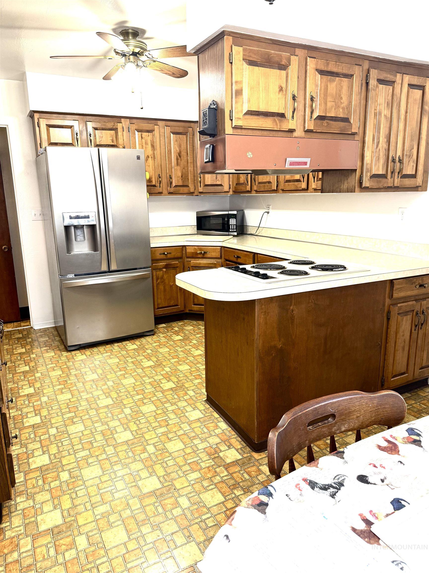 Kitchen featuring a peninsula, light countertops, stainless steel appliances, brown cabinets, and ceiling fan