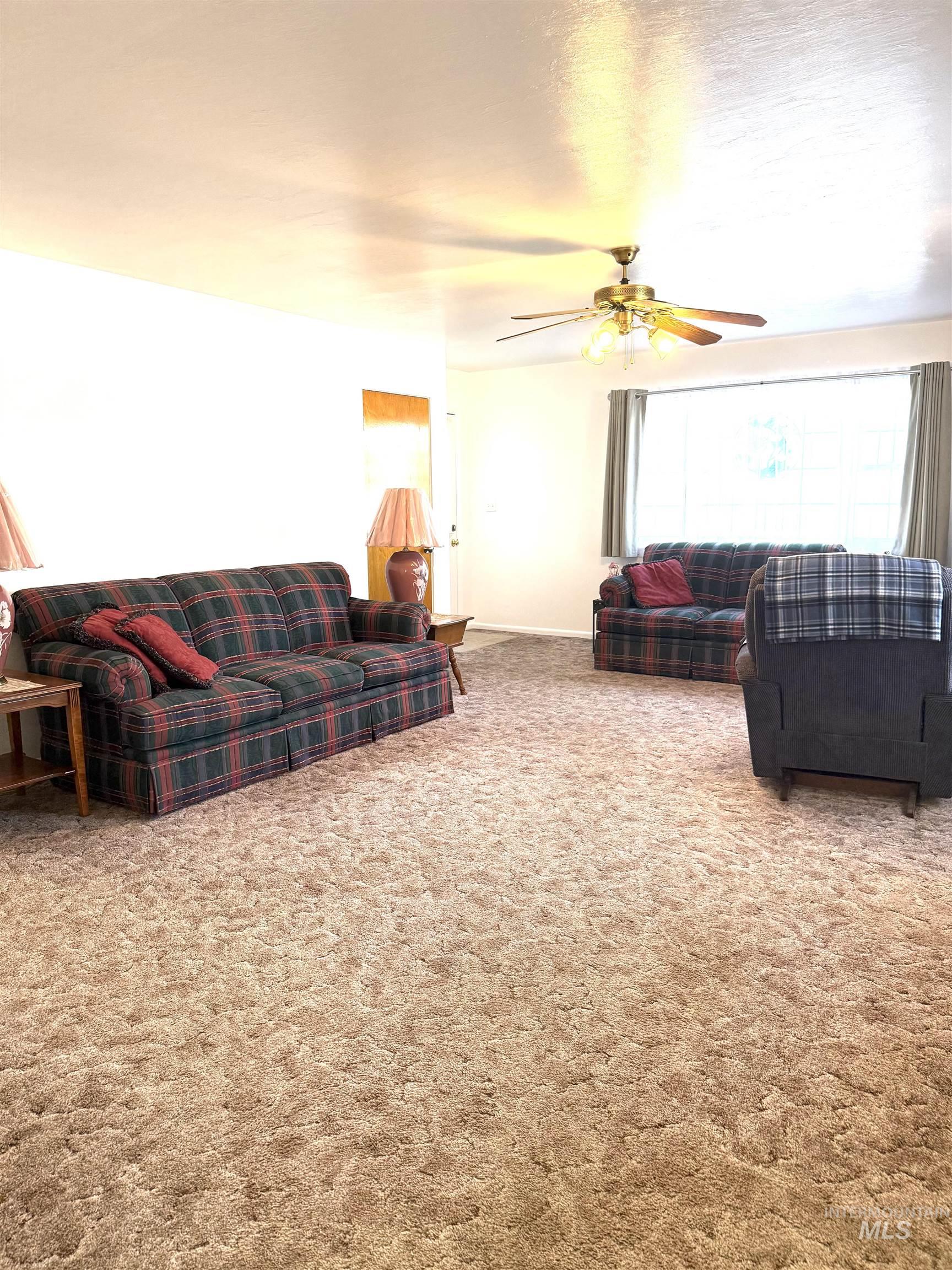 Carpeted living area with ceiling fan and baseboards