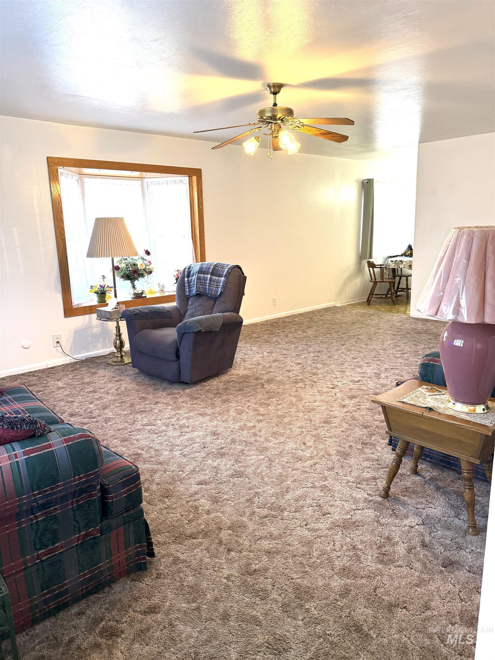 Carpeted living room with a ceiling fan and baseboards