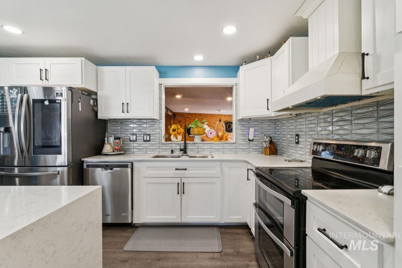 Kitchen with appliances with stainless steel finishes, white cabinetry, light stone counters, dark wood-style floors, and backsplash