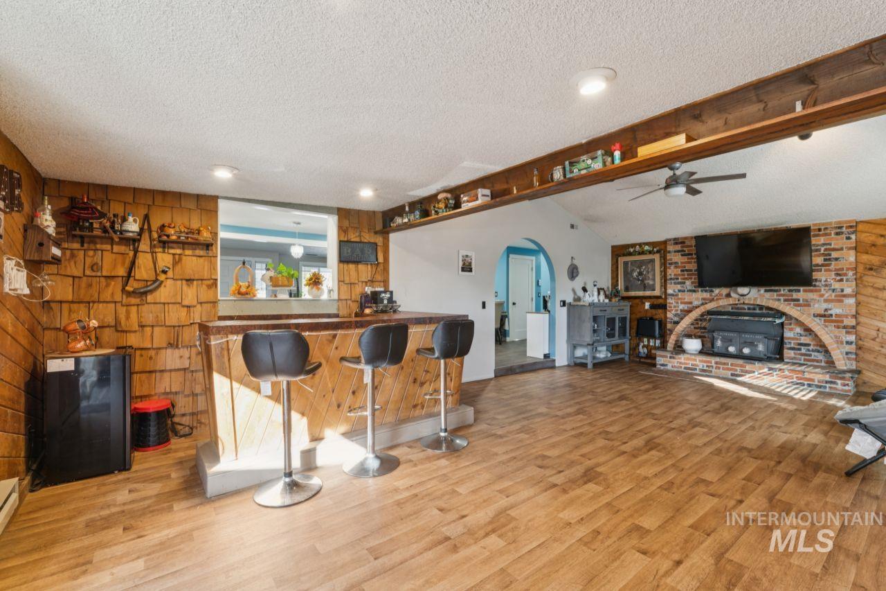 Indoor dry bar featuring wooden walls, a textured ceiling, light wood-style flooring, ceiling fan, and arched walkways