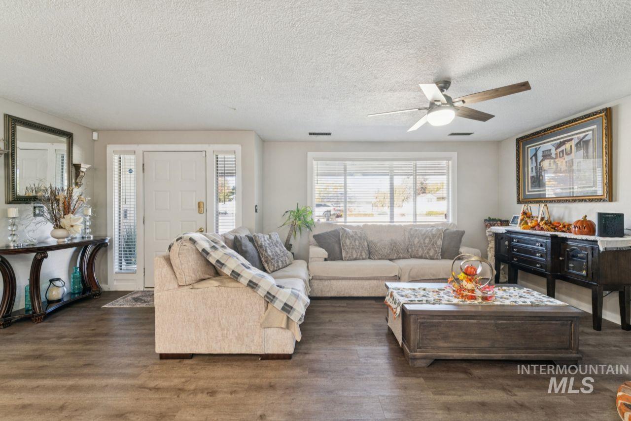 Living room with a textured ceiling, dark wood-type flooring, and a ceiling fan