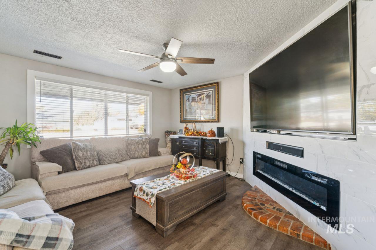 Living room with a glass covered fireplace, wood finished floors, a textured ceiling, and a ceiling fan