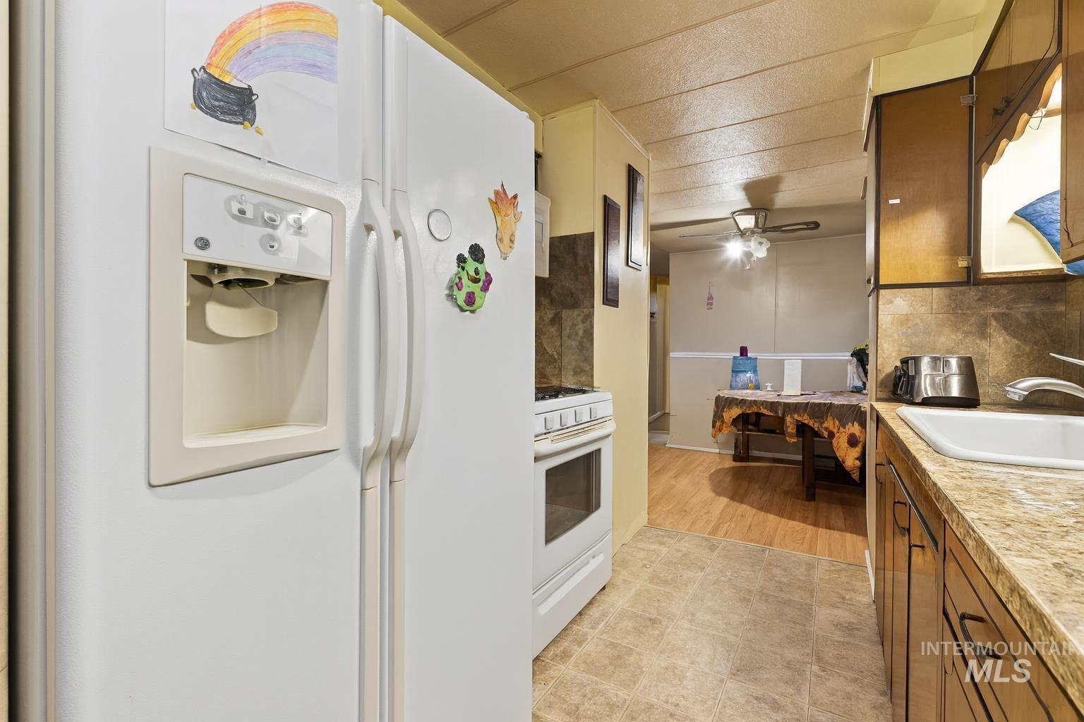 Kitchen featuring white appliances, backsplash, brown cabinetry, light countertops, and a ceiling fan