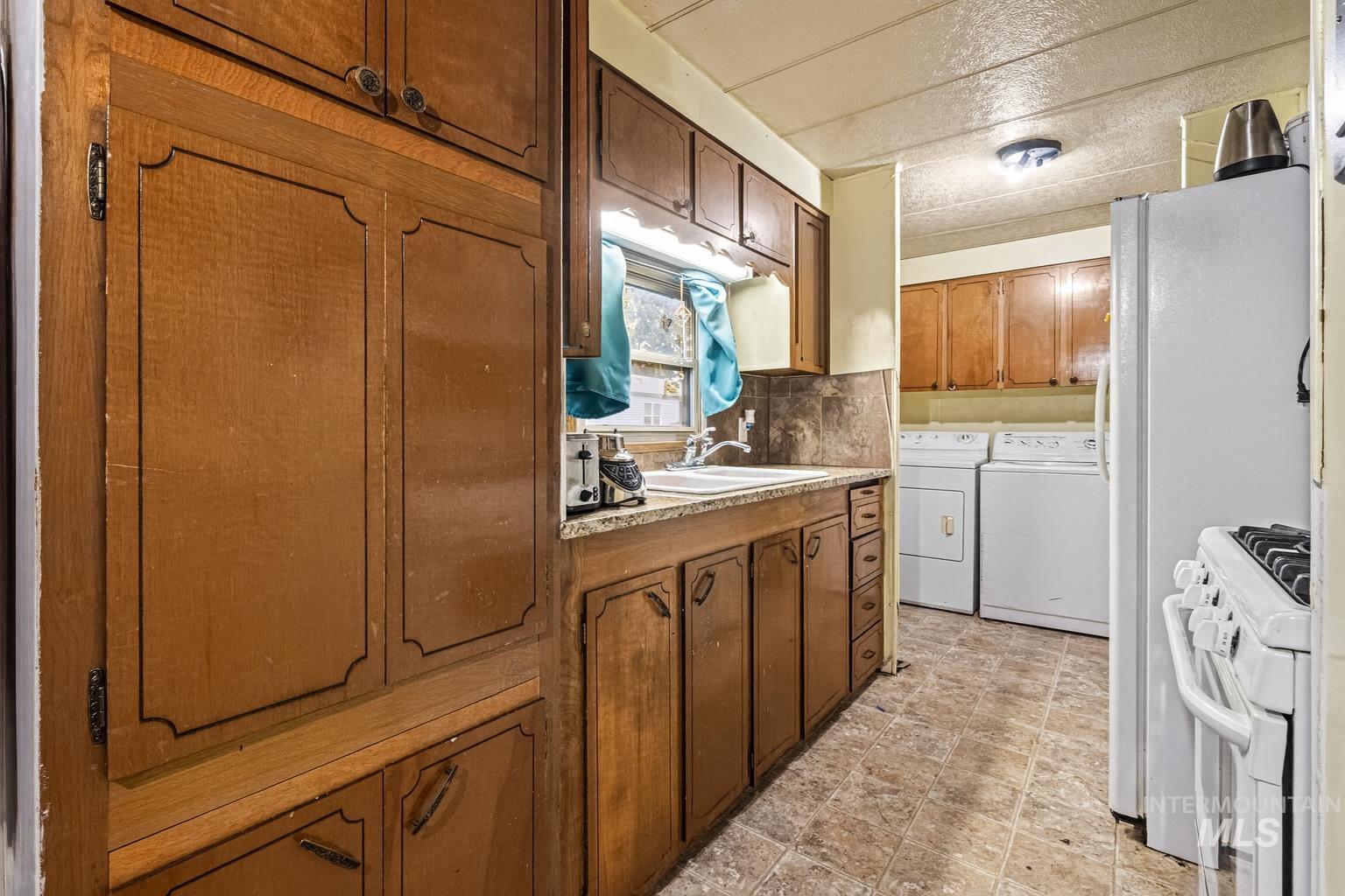 Kitchen with white range with gas cooktop, backsplash, light countertops, washer and clothes dryer, and brown cabinets