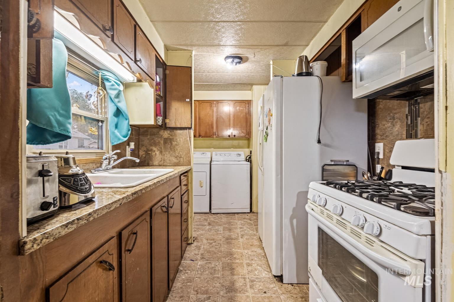 Kitchen with white appliances, independent washer and dryer, brown cabinets, and light countertops