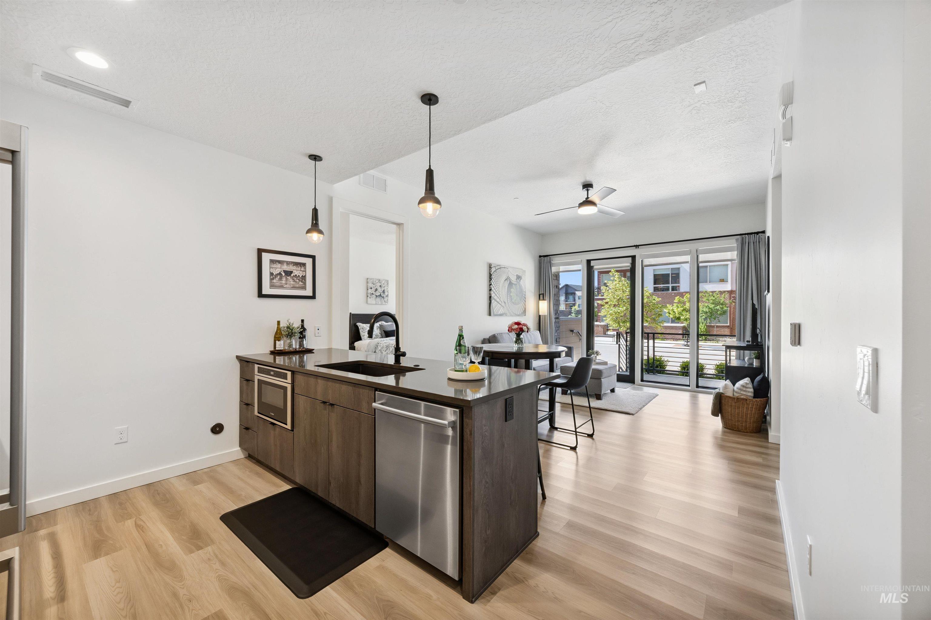 Kitchen with modern cabinets, dark brown cabinets, hanging light fixtures, a peninsula, and light wood-type flooring