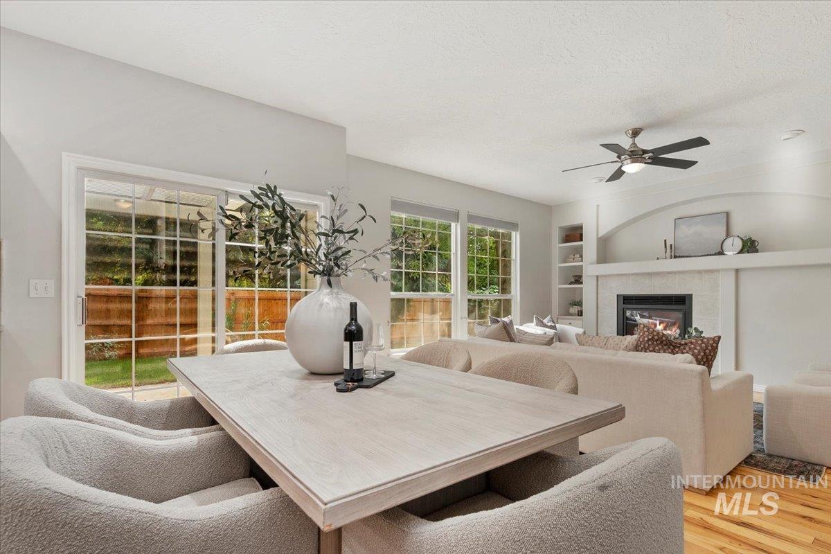 Dining area featuring built in shelves, a textured ceiling, a tile fireplace, a ceiling fan, and light wood-style floors