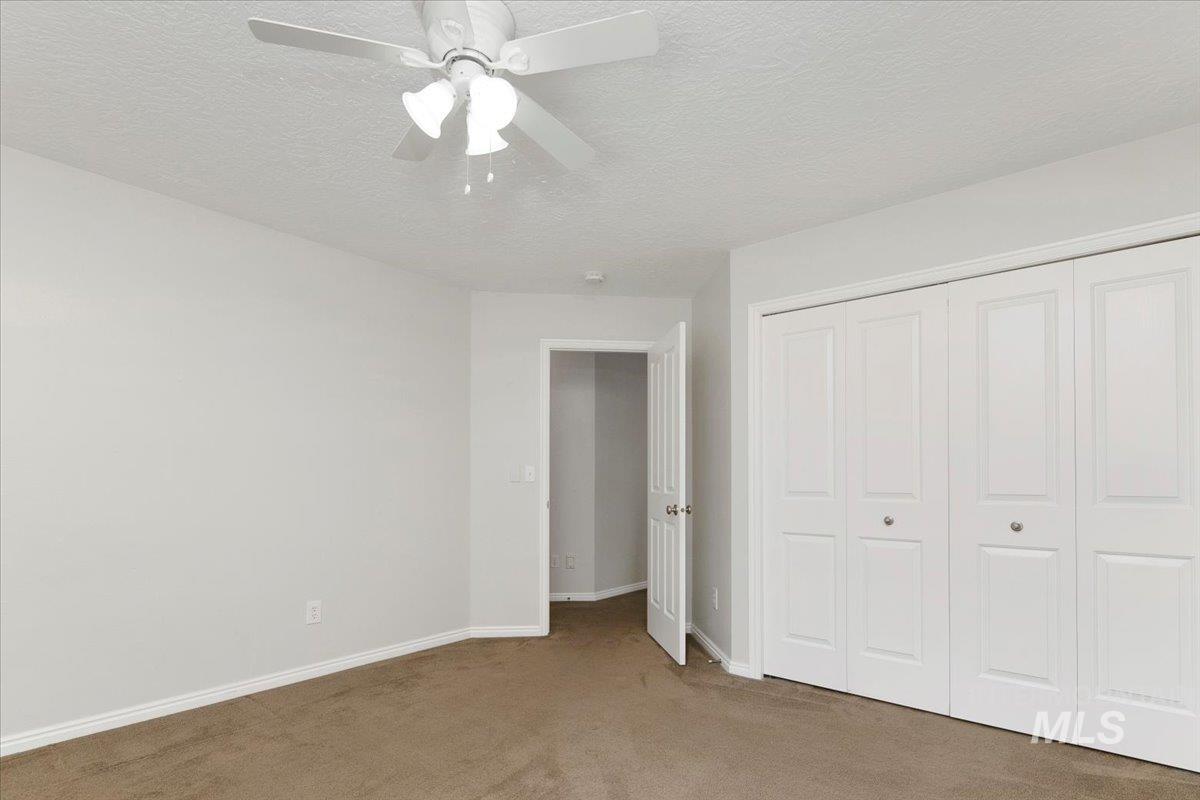 Unfurnished bedroom featuring carpet floors, a textured ceiling, a closet, and a ceiling fan