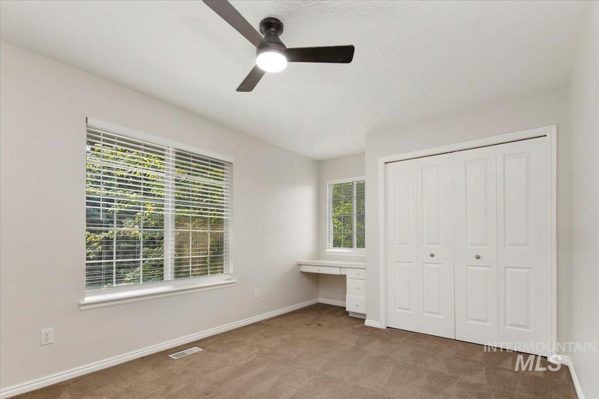 Unfurnished bedroom featuring carpet, built in study area, a ceiling fan, a closet, and a textured ceiling