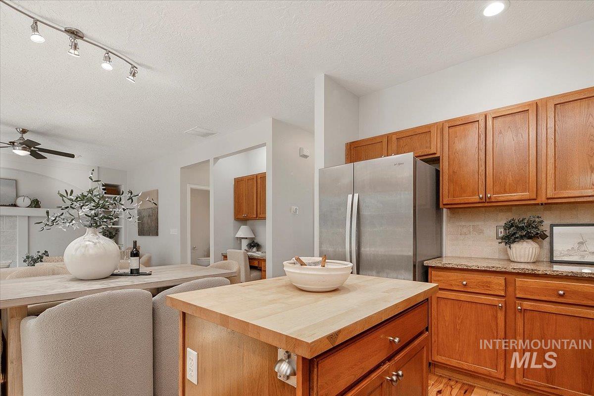 Kitchen with wooden counters, freestanding refrigerator, brown cabinets, backsplash, and a textured ceiling