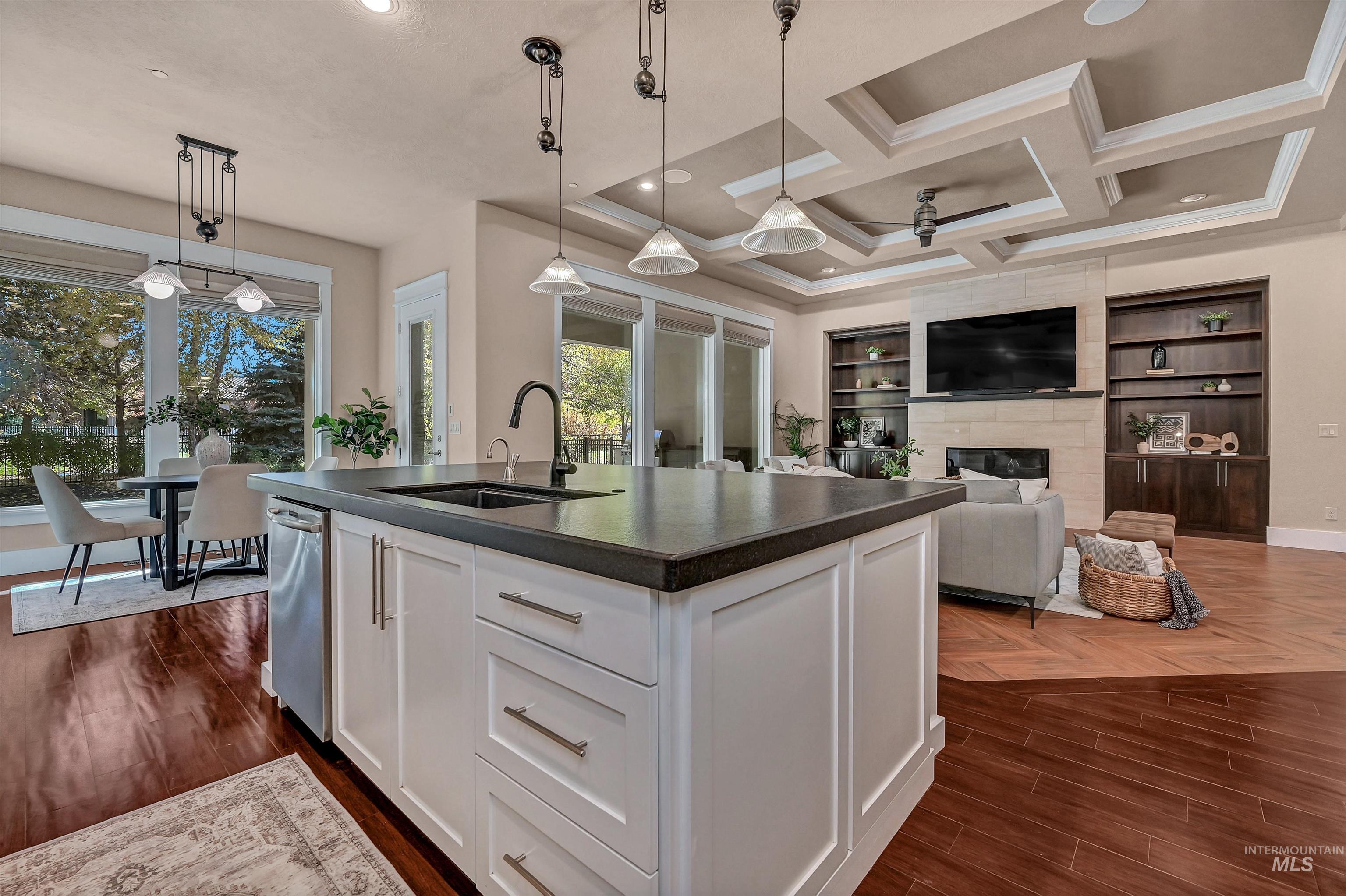 Kitchen featuring white cabinetry, pendant lighting, a center island with sink, a large fireplace, and coffered ceiling