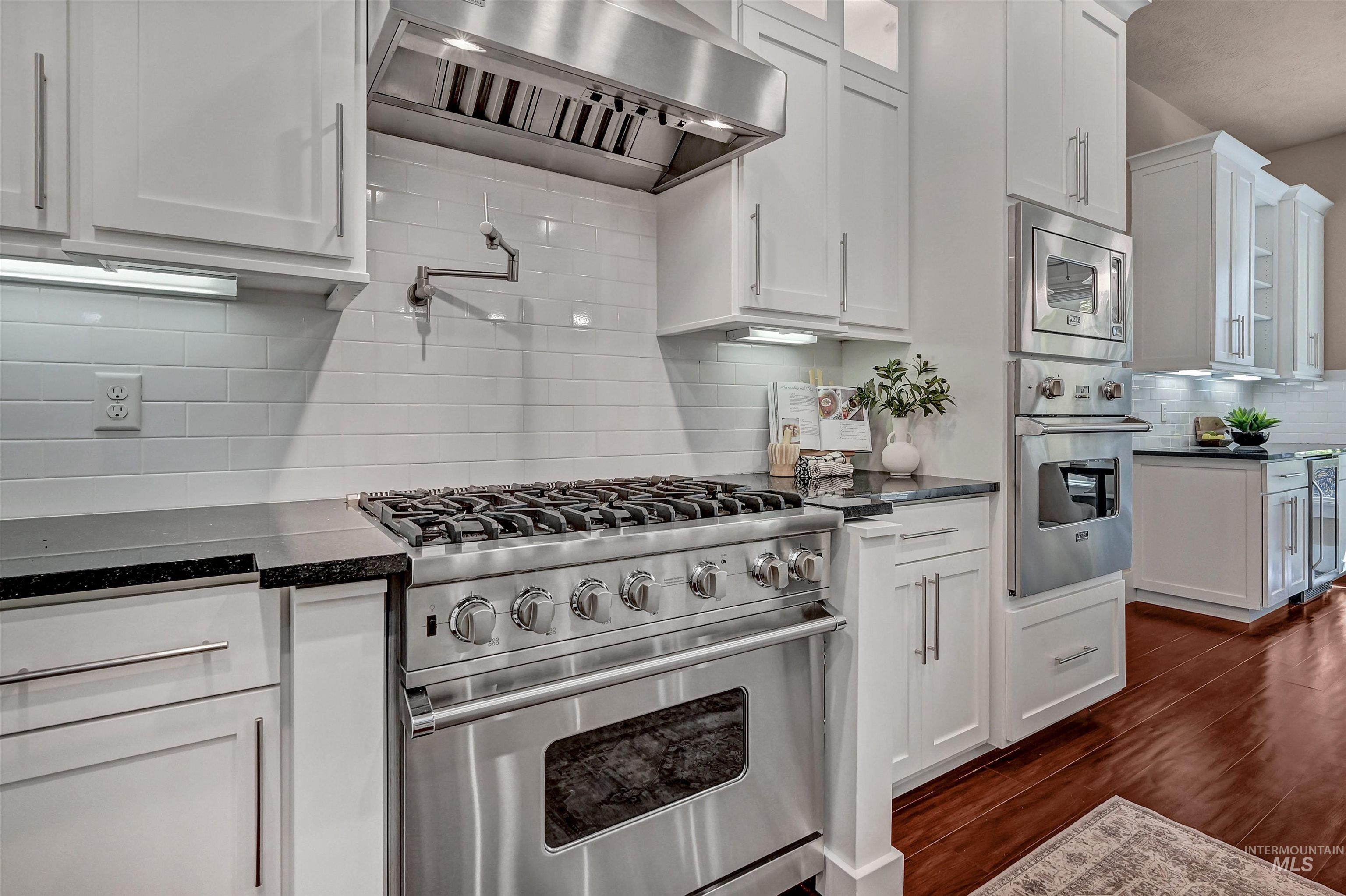 Kitchen featuring backsplash, wall chimney range hood, glass insert cabinets, stainless steel appliances, and white cabinetry