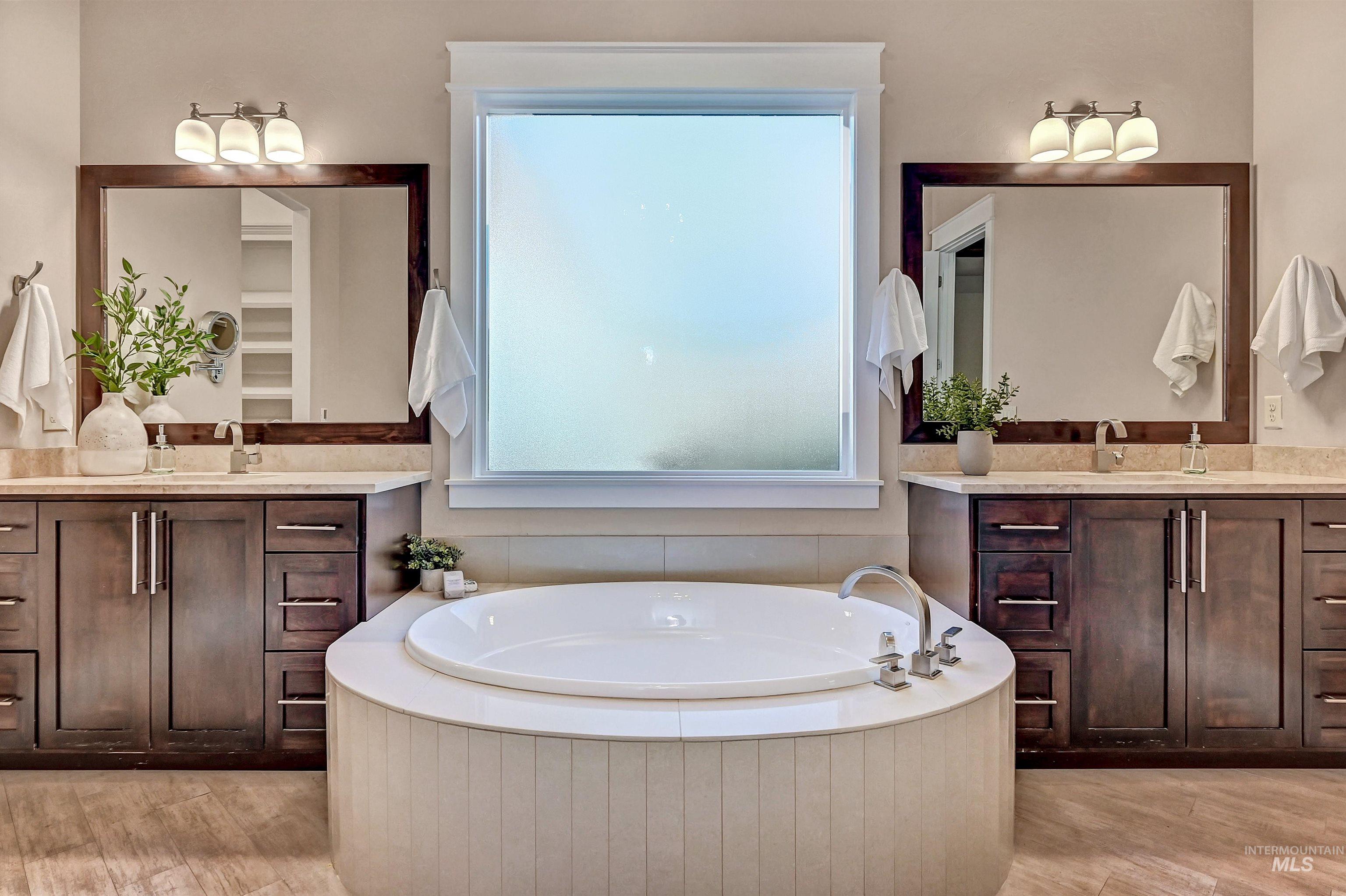 Full bath with two vanities, a garden tub, and light wood finished floors