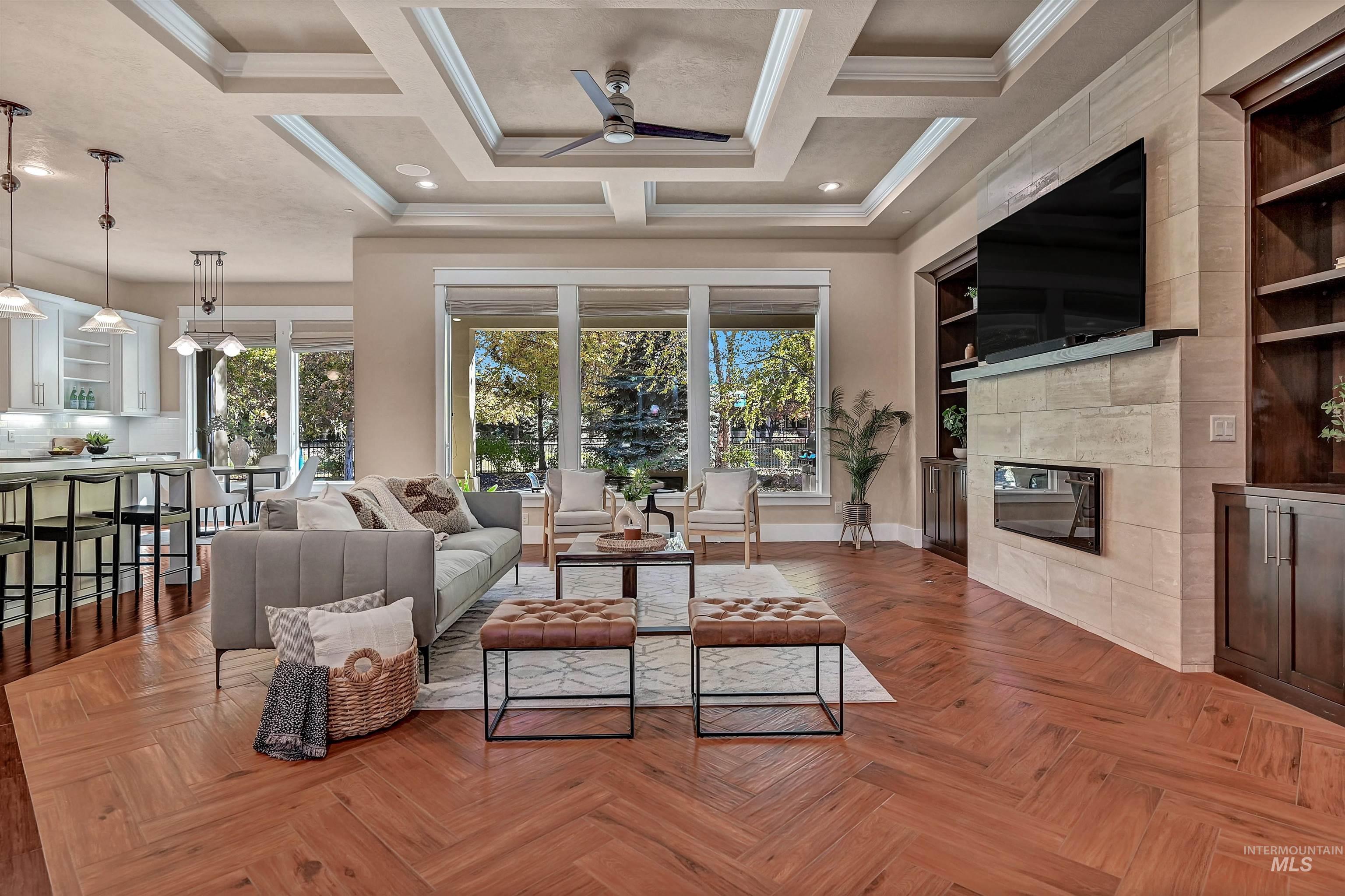 Living room featuring ceiling fan, ornamental molding, a fireplace, coffered ceiling, and beam ceiling