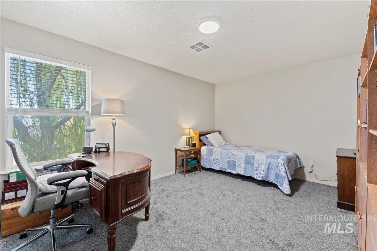 Bedroom with an office area, light colored carpet, and a textured ceiling