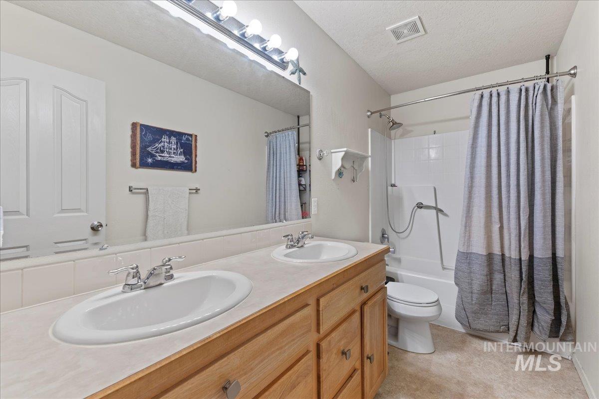 Bathroom with double vanity, shower / tub combo with curtain, and a textured ceiling