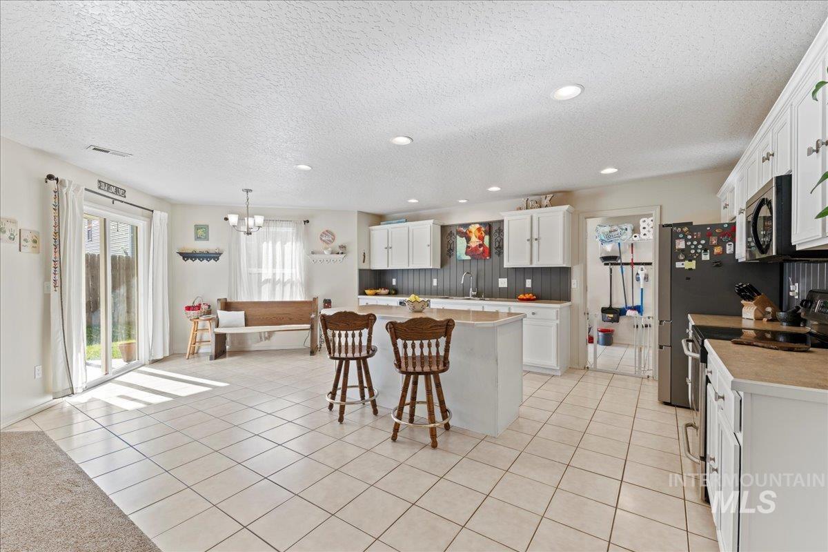 Kitchen featuring light countertops, stainless steel appliances, light tile patterned floors, white cabinets, and a textured ceiling