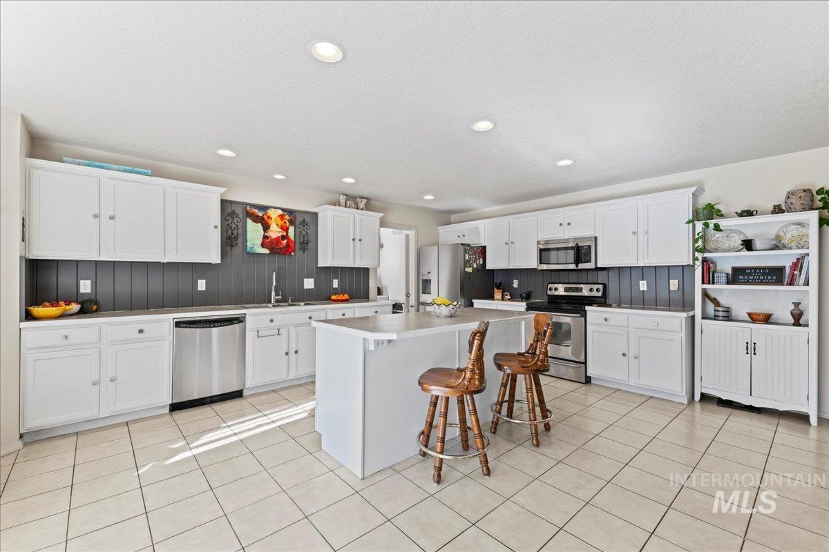 Kitchen featuring a kitchen bar, white cabinetry, appliances with stainless steel finishes, light tile patterned floors, and recessed lighting