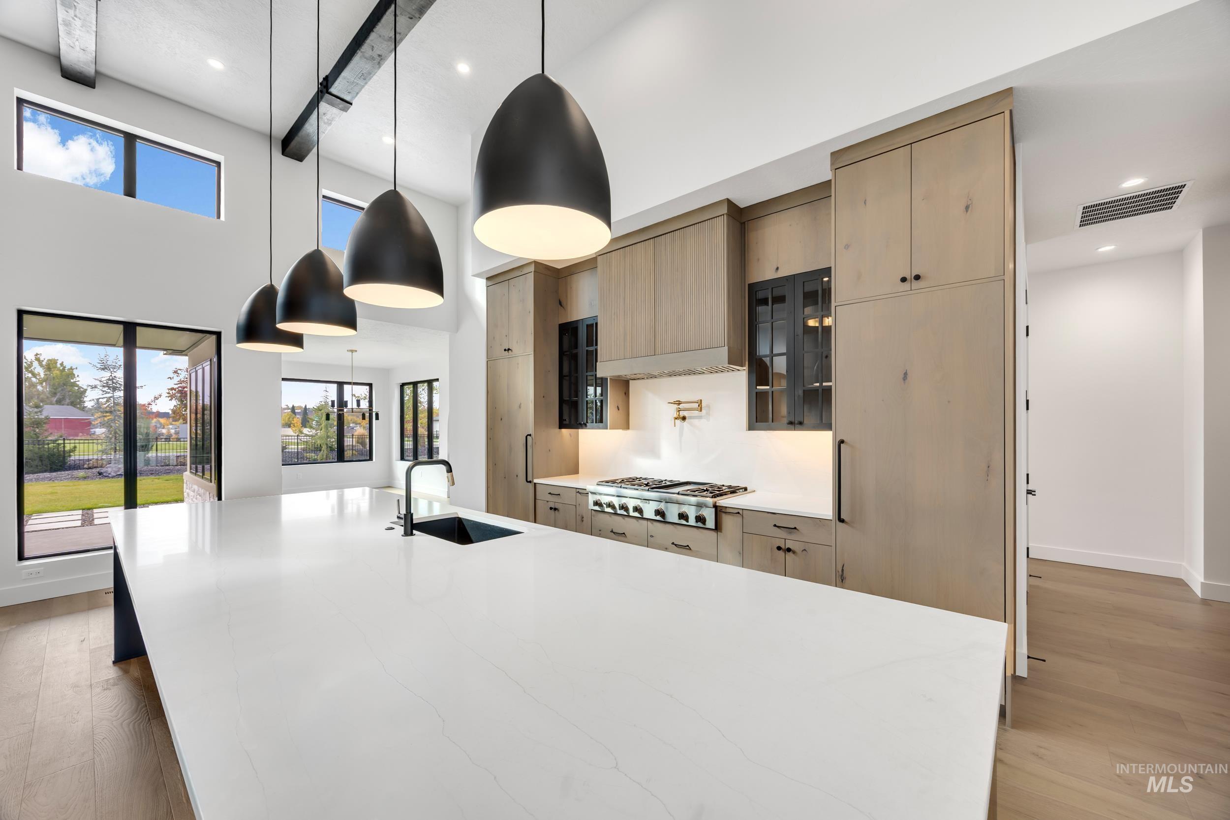 Kitchen with hanging light fixtures, light wood-type flooring, light stone countertops, a large island, and glass insert cabinets