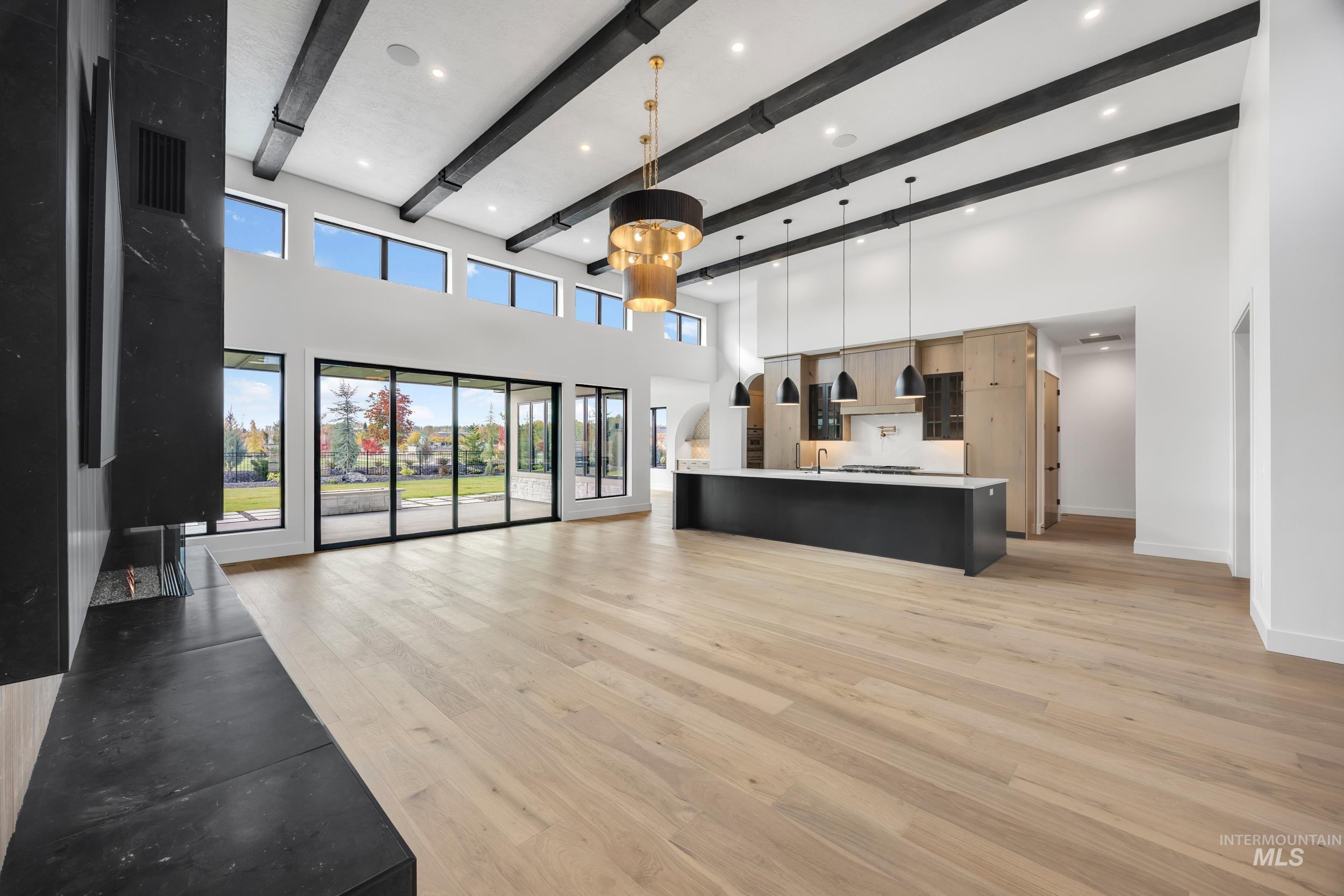 Unfurnished living room with light wood-type flooring, beamed ceiling, a towering ceiling, and recessed lighting