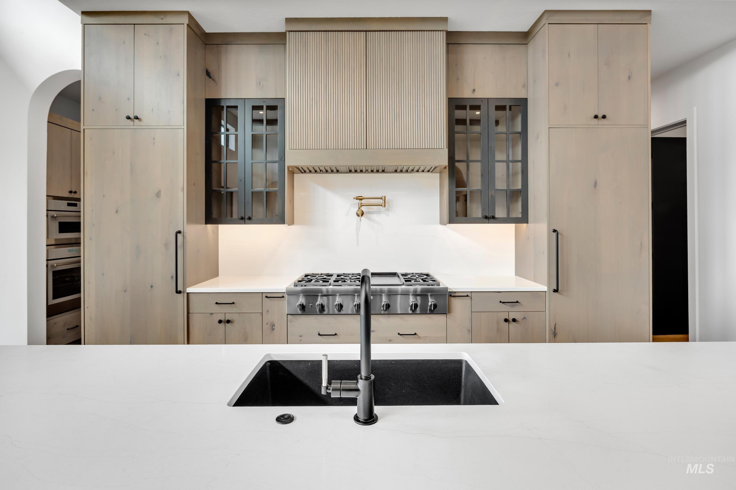Kitchen featuring light brown cabinetry, glass insert cabinets, range hood, and light stone countertops