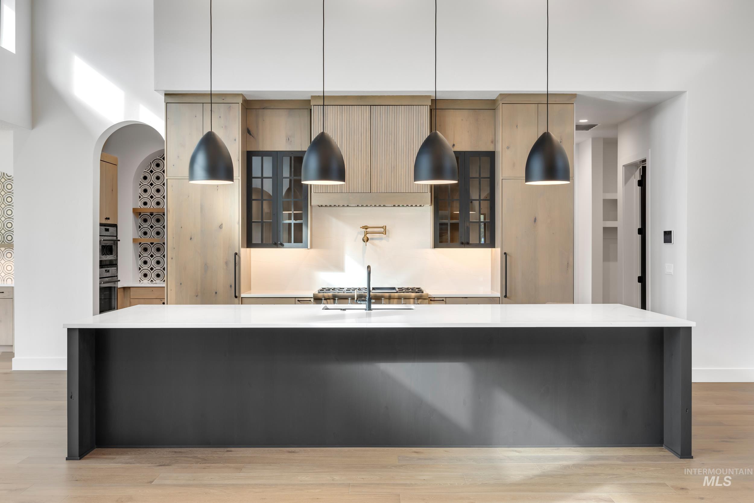 Kitchen with glass insert cabinets, a spacious island, decorative light fixtures, light stone countertops, and light wood finished floors