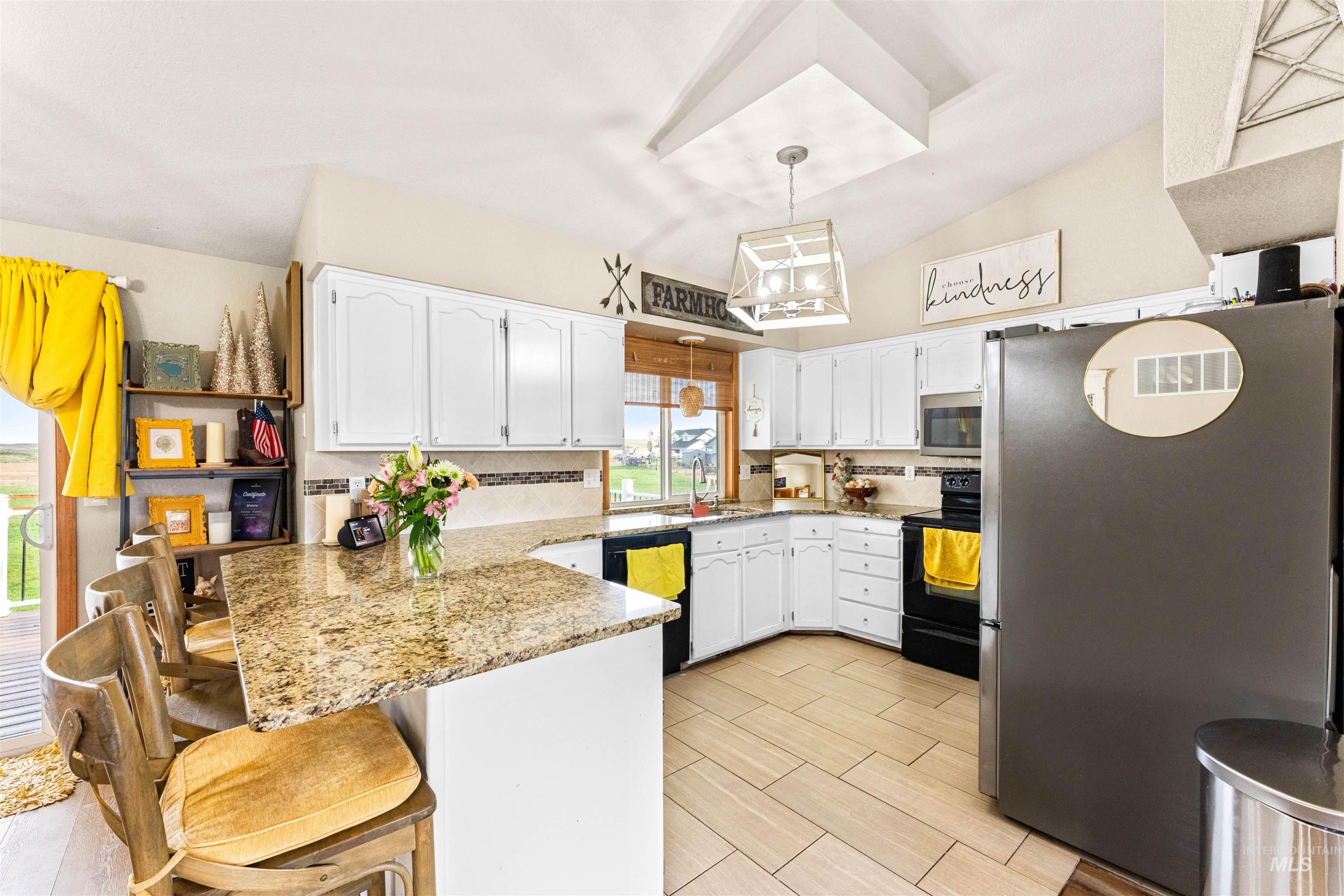Kitchen featuring a peninsula, black appliances, a breakfast bar, white cabinets, and hanging light fixtures