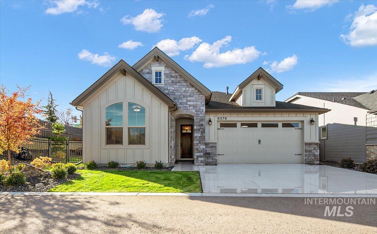 View of front facade with board and batten siding, stone siding, driveway, and an attached garage