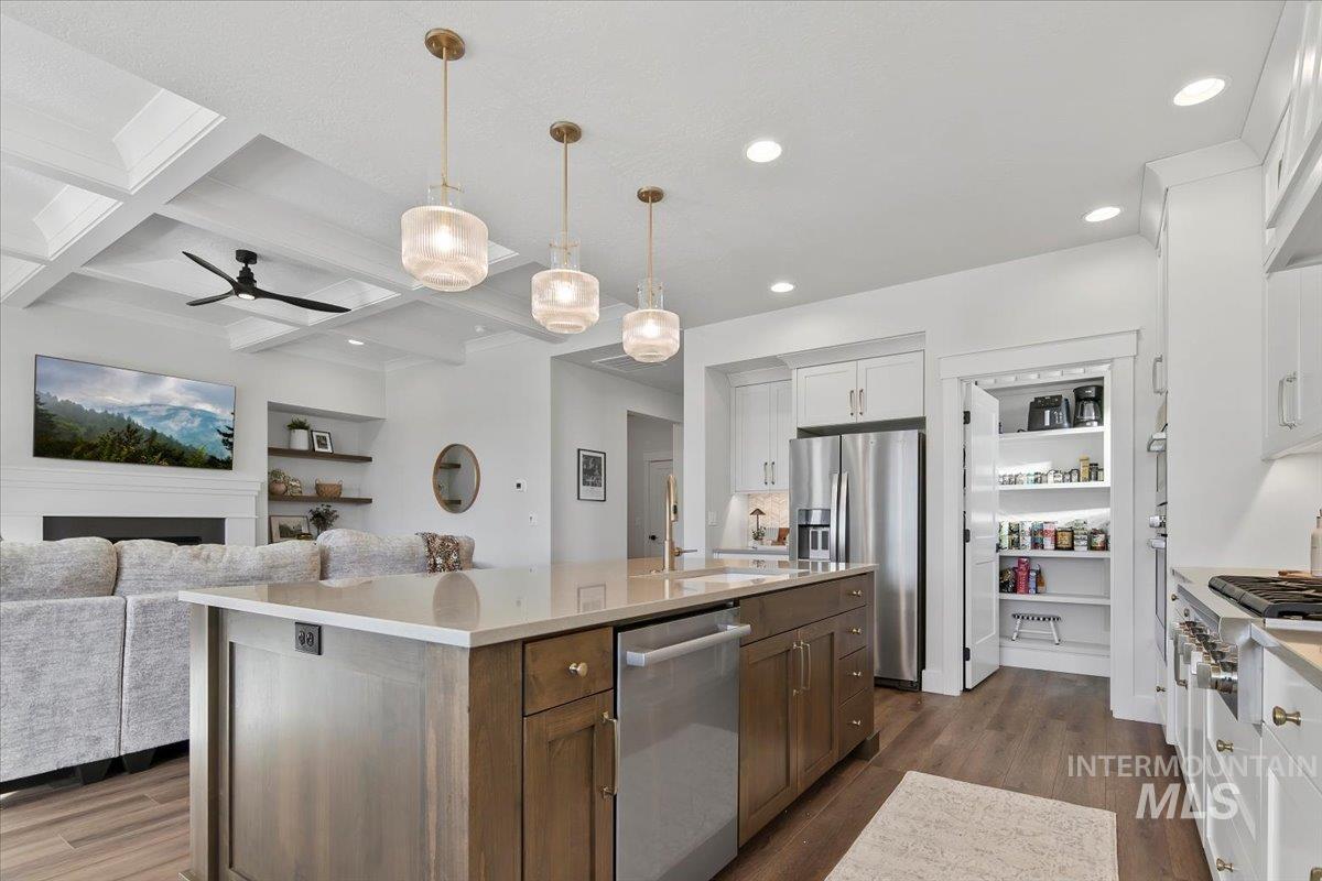 Kitchen with dark wood finished floors, stainless steel appliances, beam ceiling, open floor plan, and hanging light fixtures