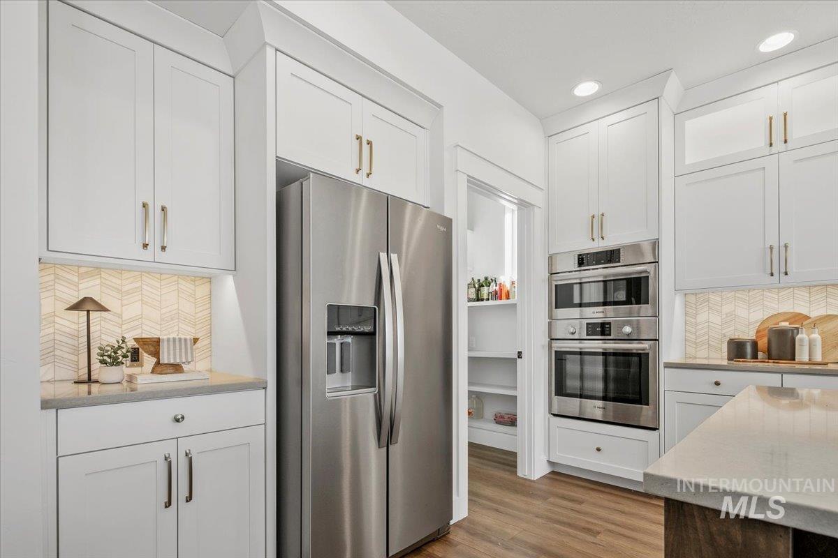 Kitchen featuring backsplash, appliances with stainless steel finishes, white cabinets, dark wood-style floors, and light stone countertops