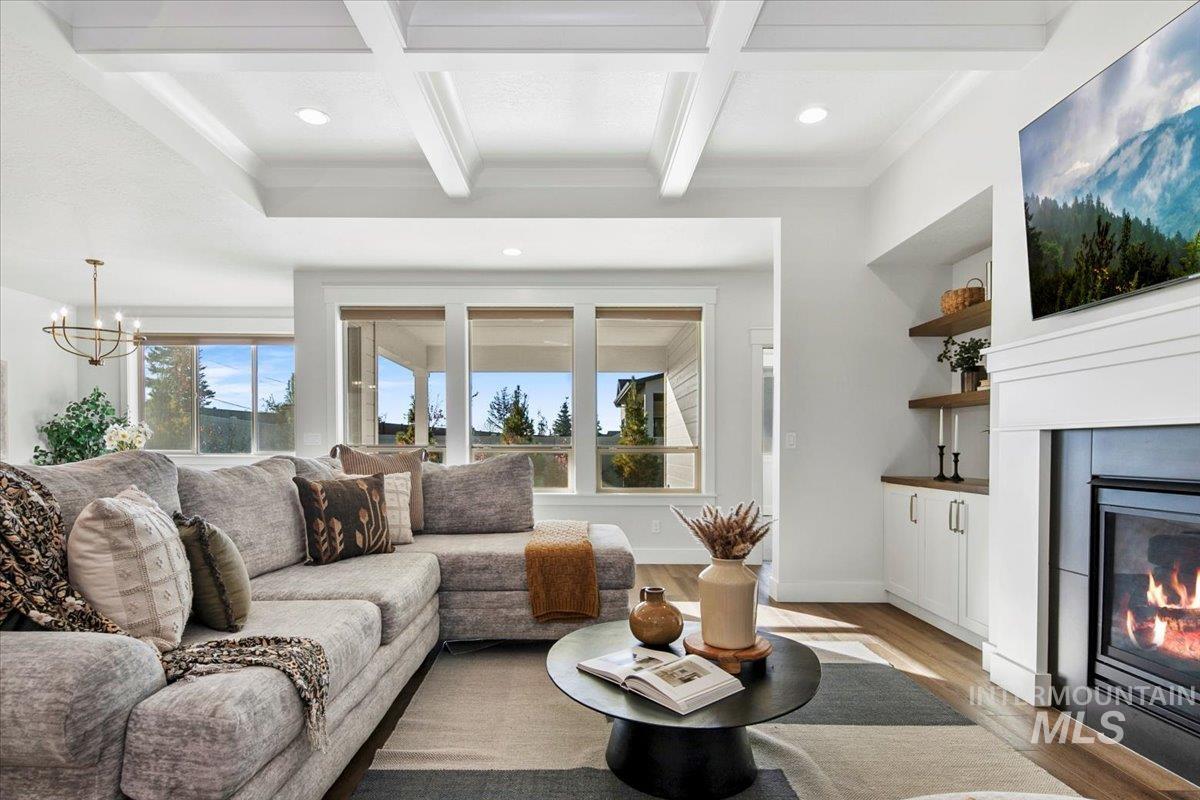 Living room featuring beamed ceiling, light wood-style flooring, recessed lighting, coffered ceiling, and a glass covered fireplace