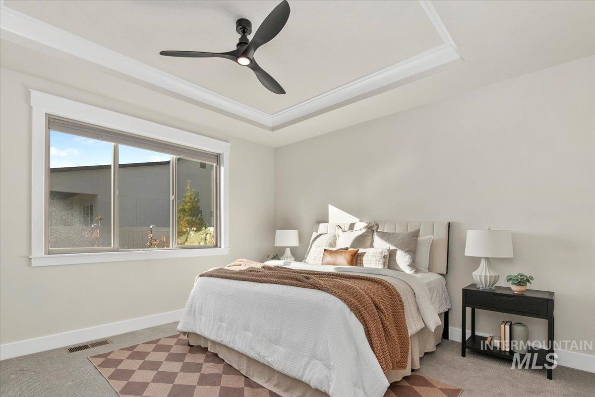 Bedroom featuring a raised ceiling, carpet flooring, and ceiling fan