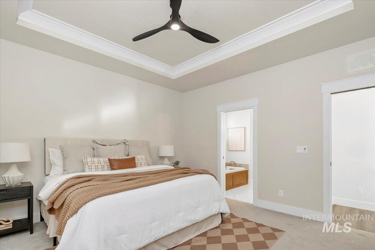 Bedroom with a raised ceiling, light carpet, ceiling fan, crown molding, and connected bathroom
