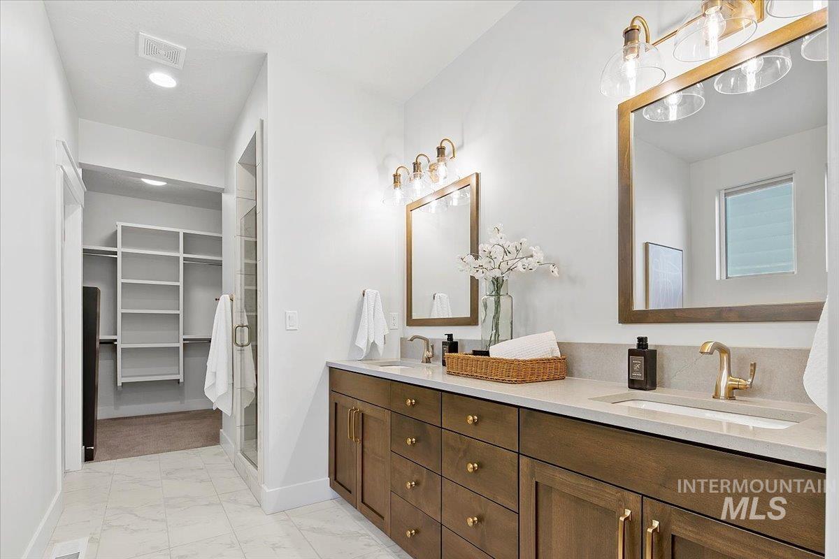 Full bath featuring double vanity, light marble finish floors, a walk in closet, and a stall shower