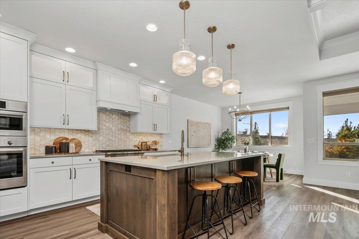 Kitchen featuring pendant lighting, a kitchen bar, wood finished floors, decorative backsplash, and white cabinets