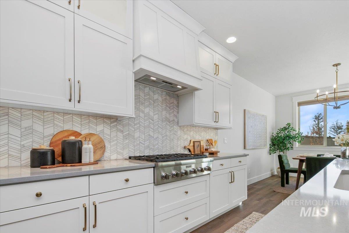 Kitchen featuring light stone countertops, tasteful backsplash, custom exhaust hood, white cabinetry, and recessed lighting