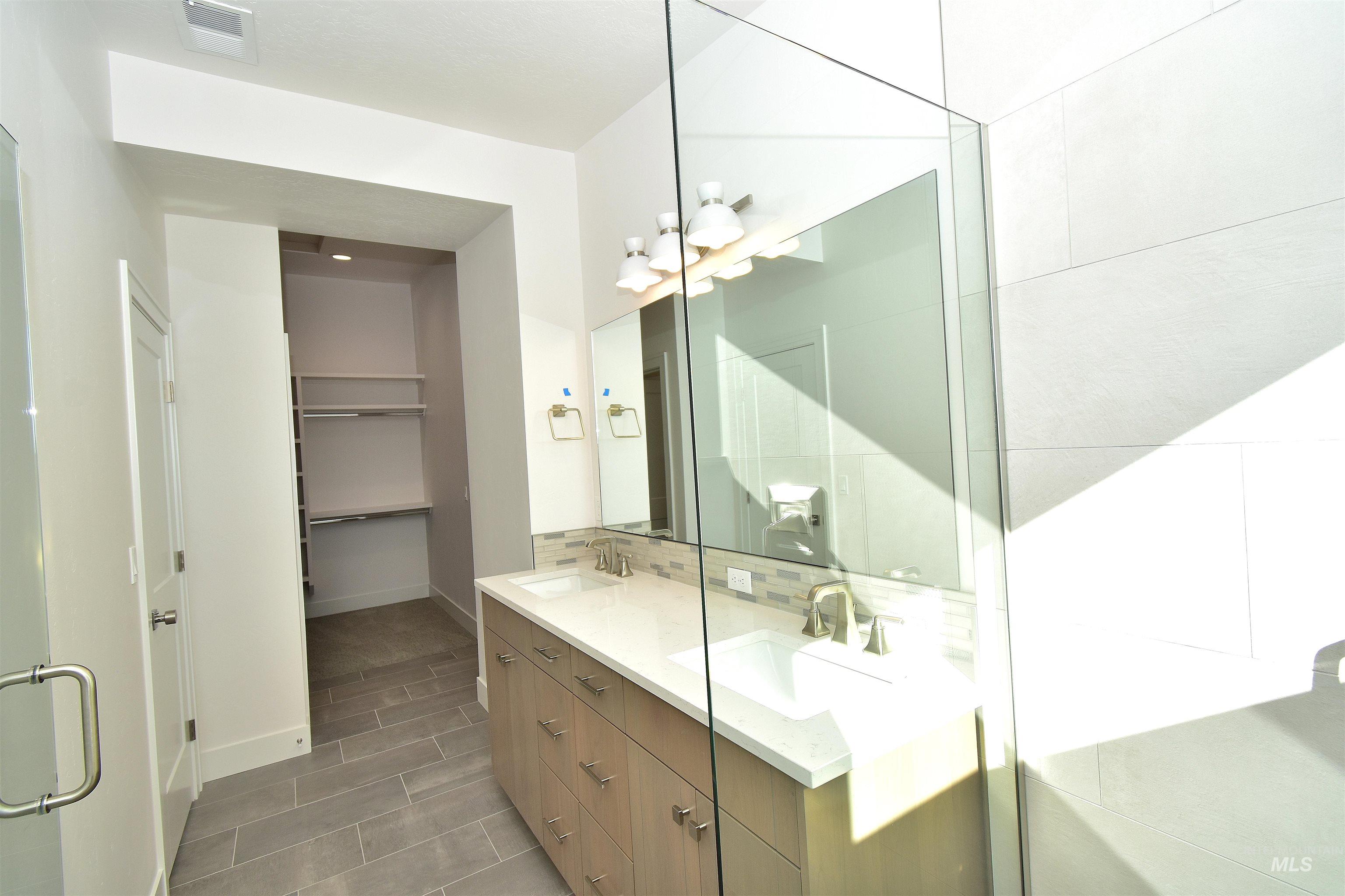 Bathroom featuring double vanity, a spacious closet, backsplash, and a shower stall