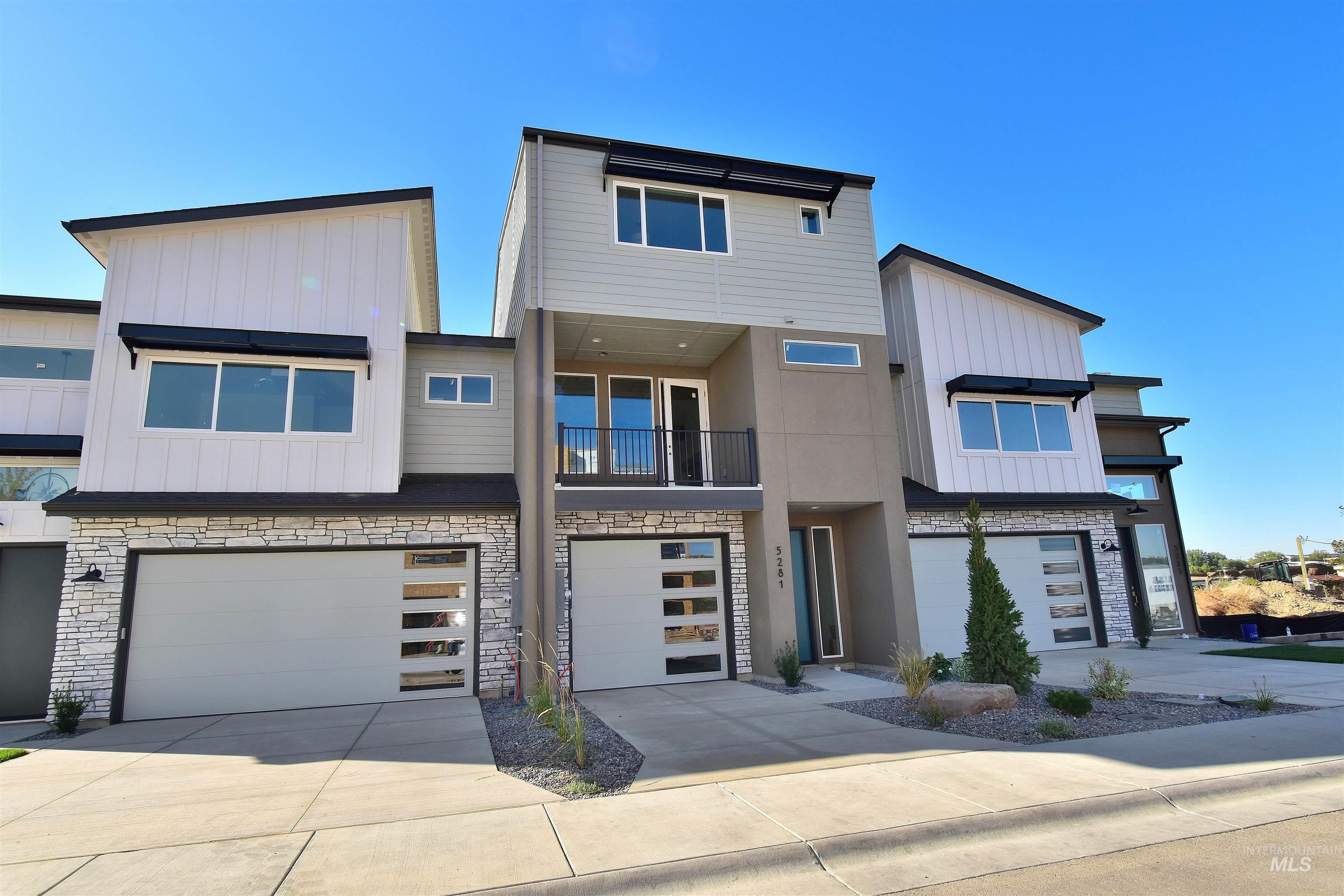 Modern home featuring stone siding, a balcony, board and batten siding, driveway, and a tandem garage