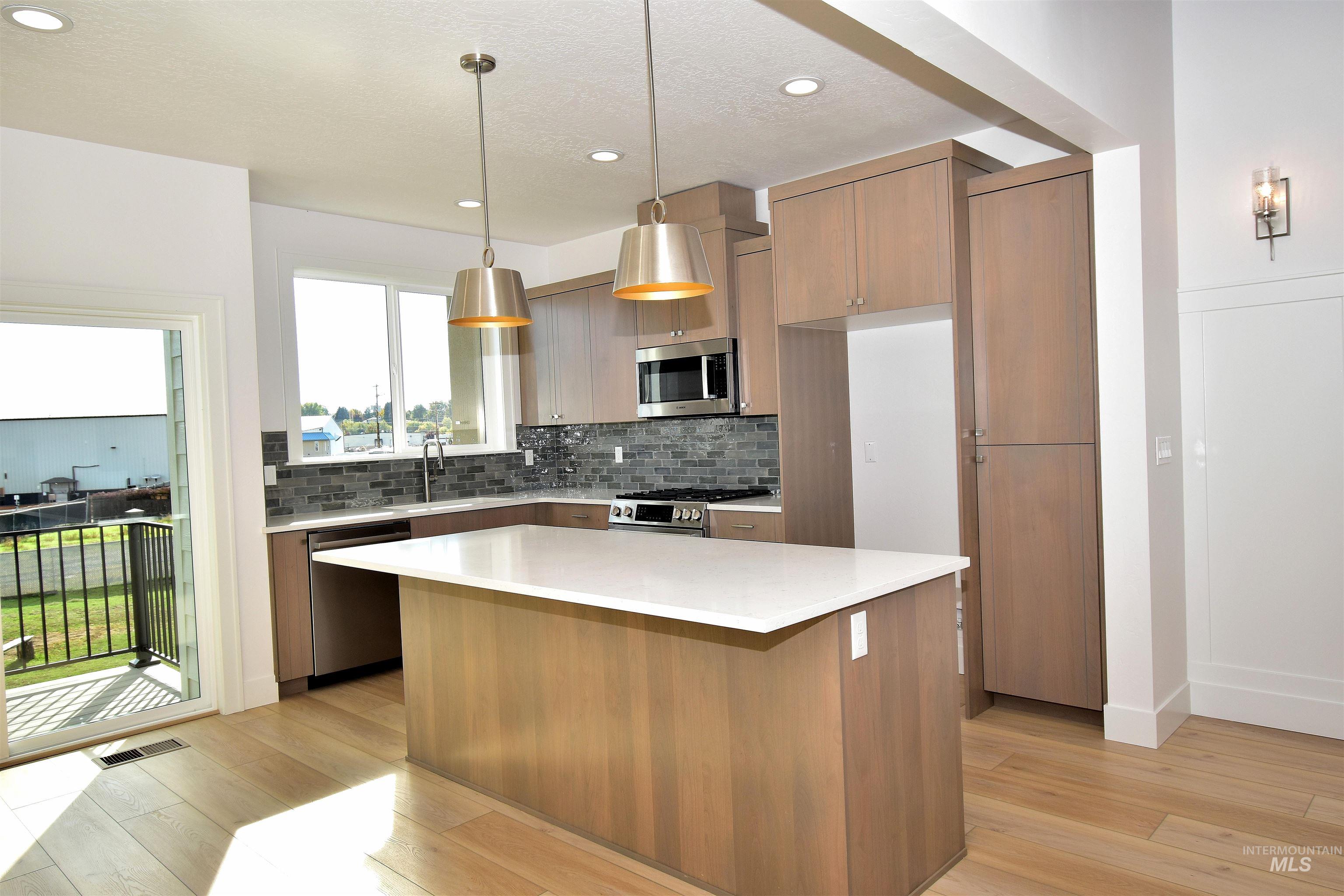 Kitchen featuring backsplash, decorative light fixtures, appliances with stainless steel finishes, light stone countertops, and light wood-style floors